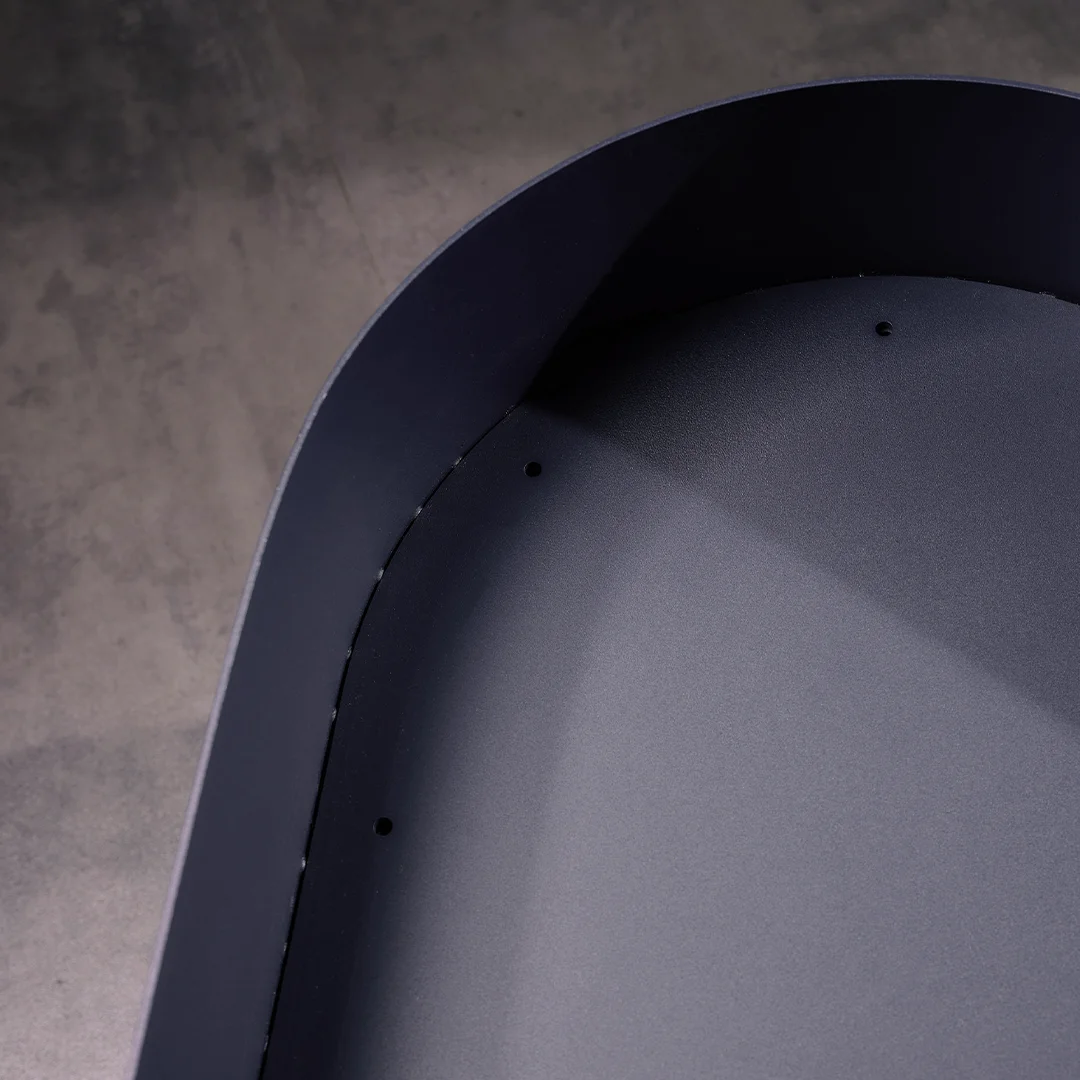 Close-up of the interior shell of a modular lounge chair, showing a smooth, curved dark surface with small drilled holes, photographed on a concrete floor.