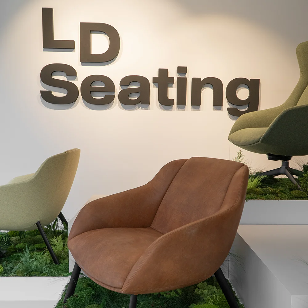 LD Seating showroom display featuring Terra Lounge armchairs in warm and muted tones, set on tiered platforms with greenery beneath a wall-mounted LD Seating logo.