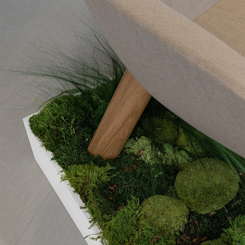 Detail of Terra Lounge armchair leg in wood set within a moss and grass installation, showing the natural, landscape-inspired display.