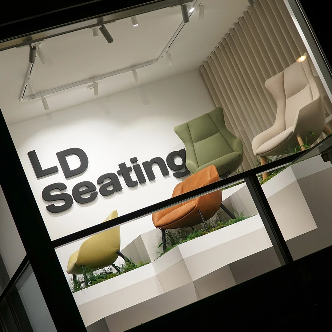 LD Seating showroom window display featuring Terra Lounge armchairs in soft, rounded forms, arranged on stepped platforms with greenery, viewed from the street at an angle.