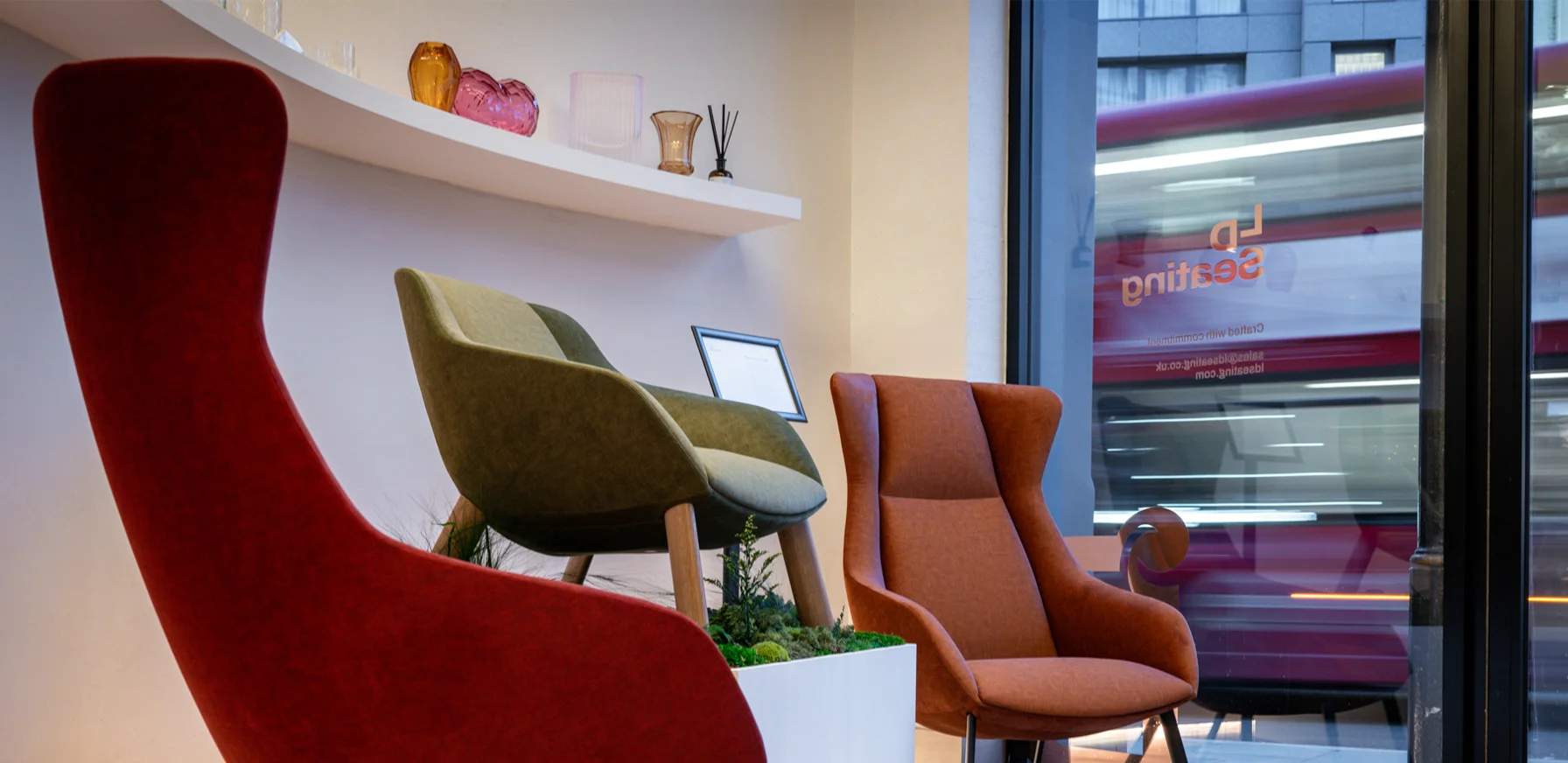 Three Terra Lounge armchairs in different colours displayed in the LD Seating London showroom beside a large street-facing window with passing city traffic outside.