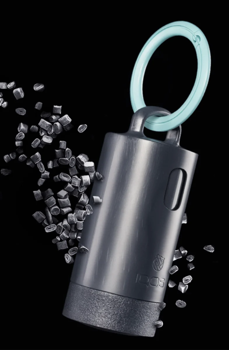 IQOS Clip Case with a turquoise carabiner shown among recycled plastic pellets and IQOS devices on a dark background.