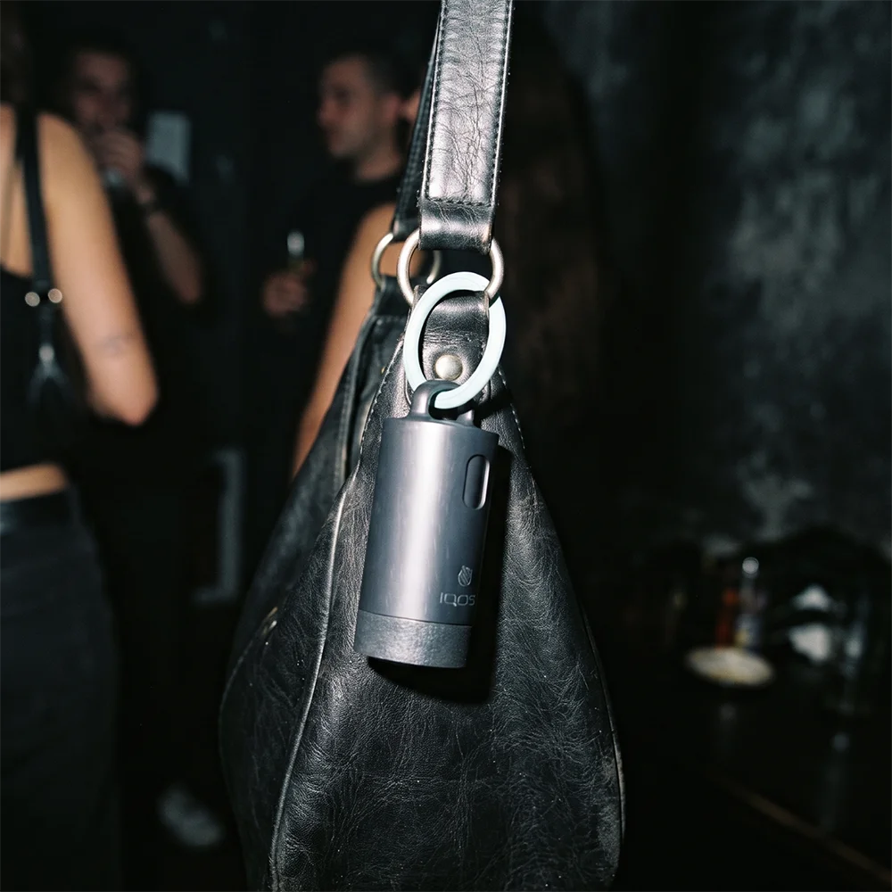 IQOS Clip Case attached to a black leather bag at an event using its turquoise ring.