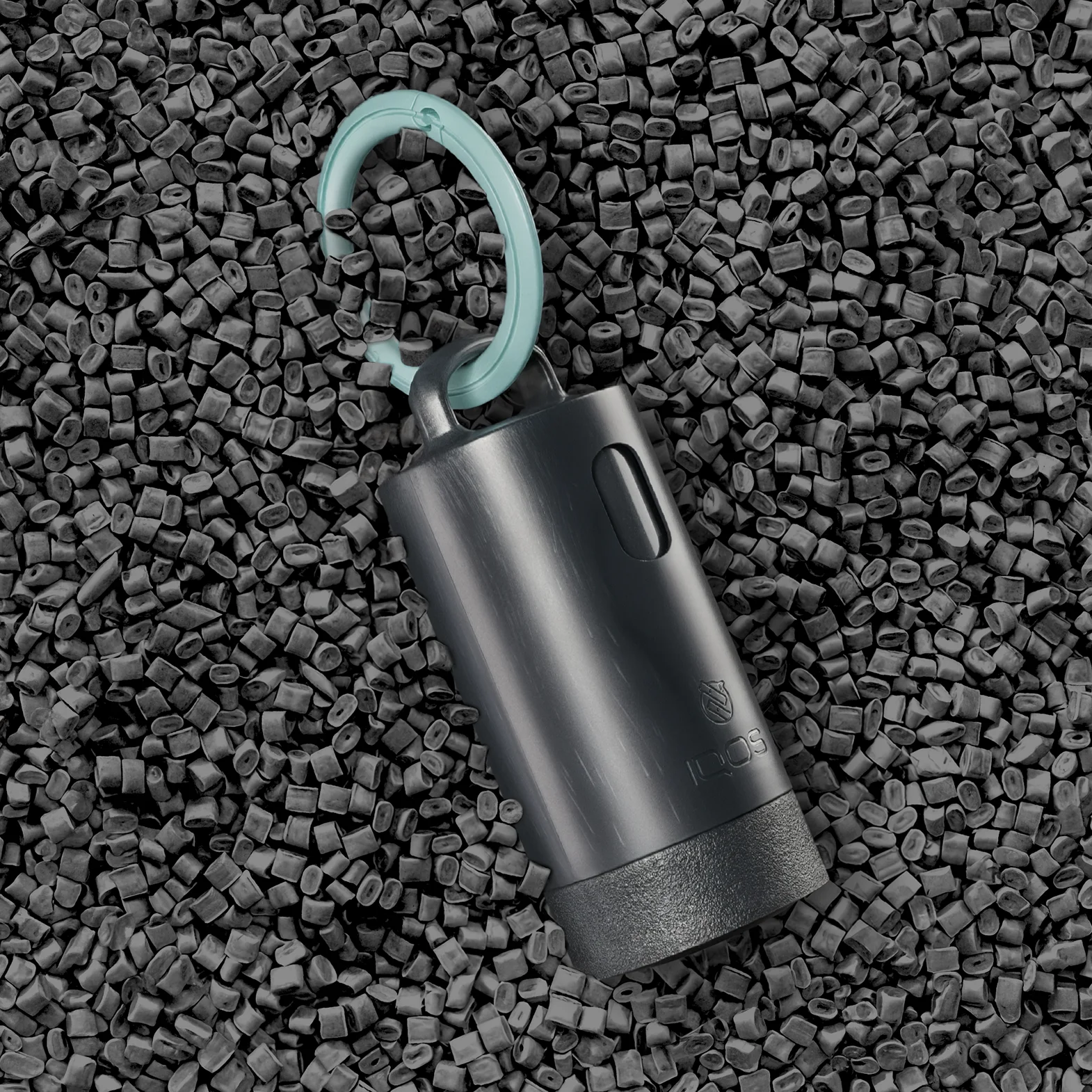 IQOS Clip Case with a turquoise carabiner, shown on recycled plastic pellets used in its production.